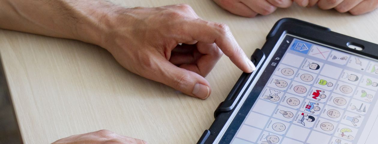 Zwei Paar Hände auf einem Tisch mit einem Tablet als Kommunikationshilfe