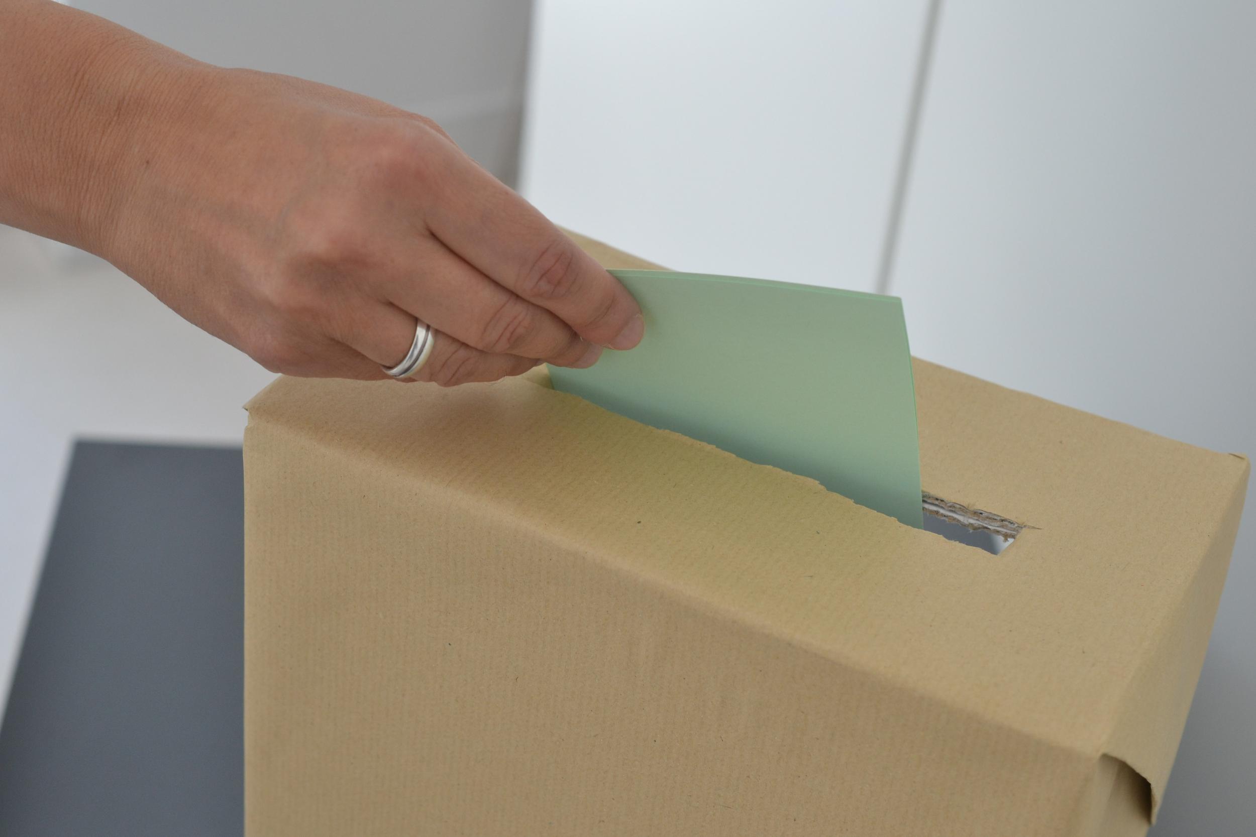 Eine Person steckt einen Zettel in eine Wahl-Urne.