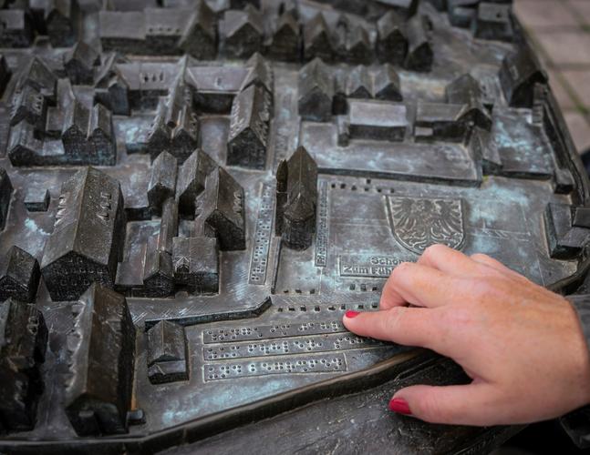 Eine Frauenhand ertastest die in Brailleschrift verfassten Erläuterungen auf einem Stadtmodell