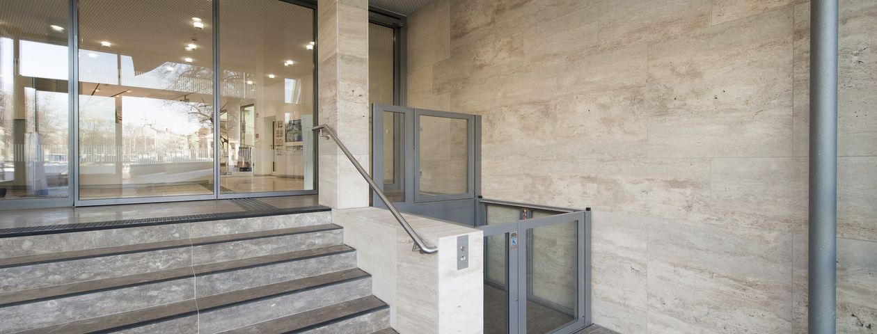 Blick auf den Eingang-Bereich des Gebäudes des Bezirks Oberbayern. Links der Treppenaufgang. Rechts die Hebeanlage für Rollstühle.