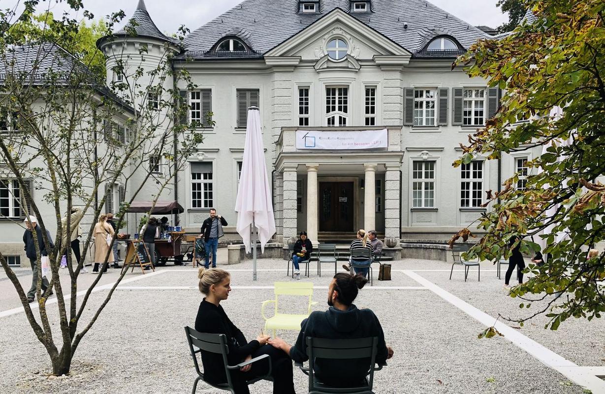 Vor dem Altbau der Bayerischen Architektenkammer sitzen einige Menschen auf Stühlen.