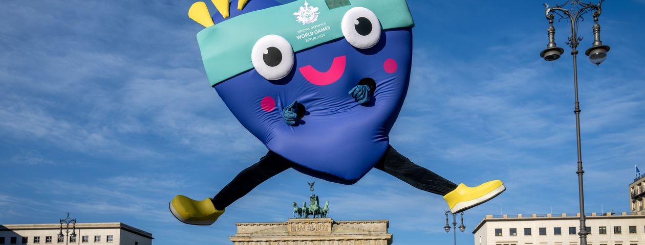 Das bunte Maskottchen der Special Olympics World Games 2023 springt vor dem Brandenburger Tor in die Luft. Es will sinnbildlich Mauern überwinden und besteht vorrangig aus einem Herz-Symbol mit Logo der Wettkämpfe.