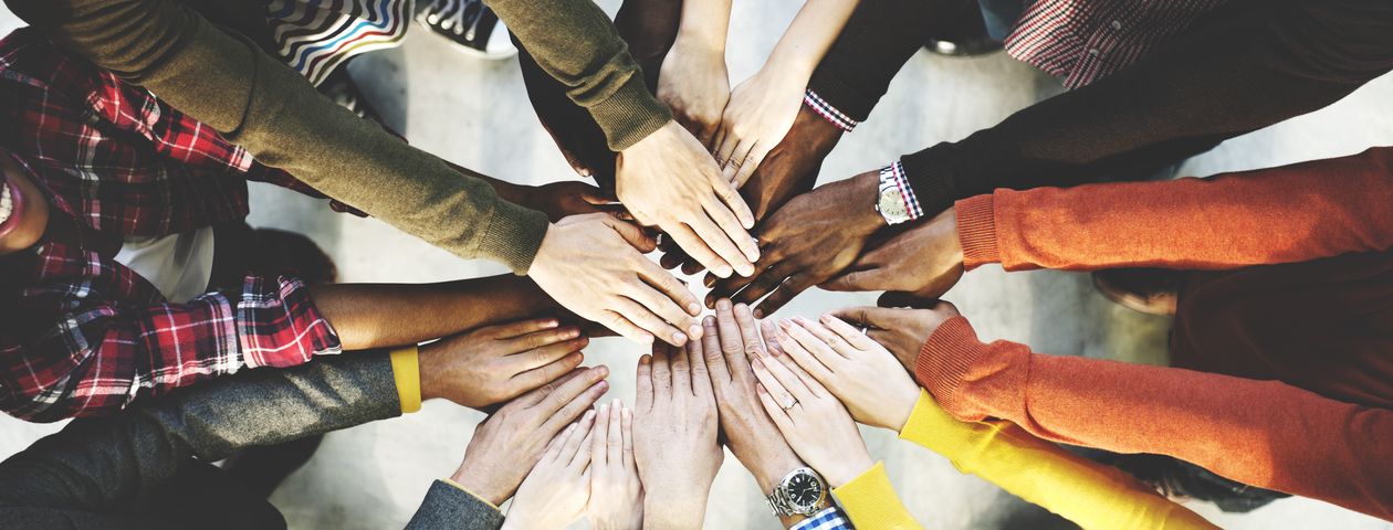 Eine multiethnische Gruppe von Menschen hält ihre Hände unterschiedlicher Hautfarben in einem Kreis übereinander 