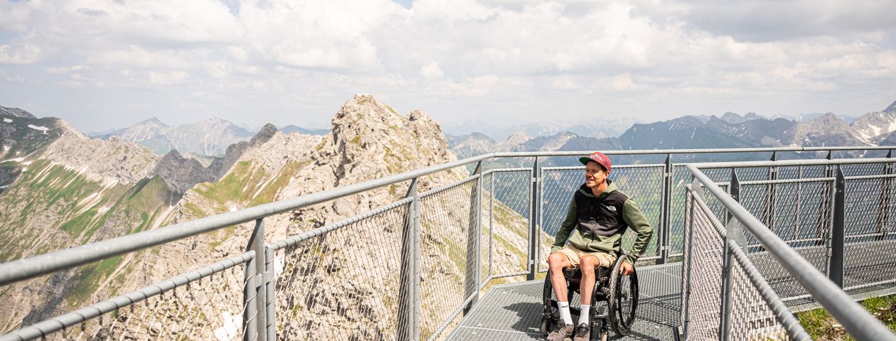 Rollstuhlfahrer fährt auf Steg mit Blick auf die Berge