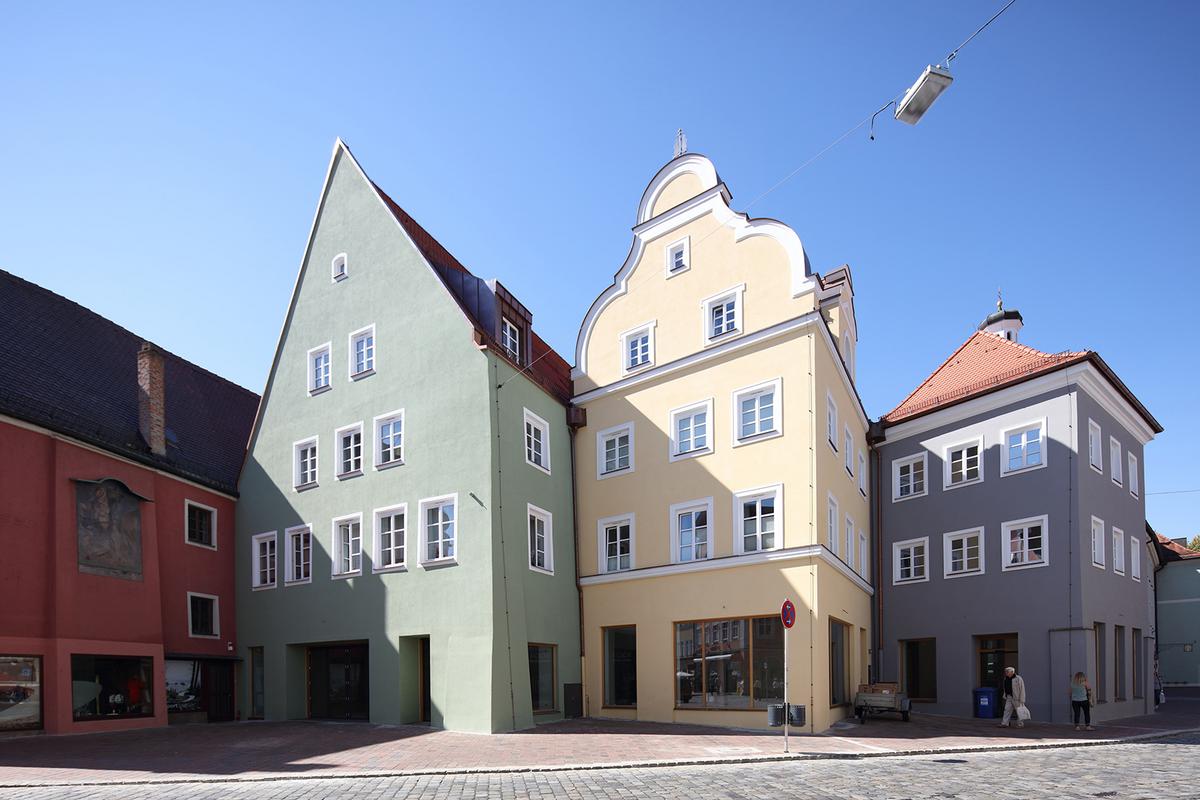 Drei sehr unterschiedliche Stadthäuser, die leicht versetzt nebeneinanderstehen. Das linke Haus mit Satteldach ist grün, das mittlere Haus mit hübschem Ziergiebel ist gelb, rechts daneben seht ein graues Haus mit Walmdach.